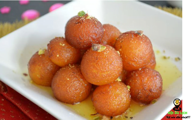 1.Món Gulab jamun Gulab jamun  là một trong những món ăn đường phố được nhiều người ưa thích tại Ấn Độ.  Nổi bật với hình tròn quả bóng siro màu vàng cánh dán, chỉ cần  nhìn thấy  là bạn sẽ bị thu hút ngay. Món này được làm từ   một loại bột nhão có thành phần chính là sữa. Những viên Gulab jamun  được nặn hình tròn đem chiên vàng và ngâm trong siro đường và cho thêm các gia vị khác như nghệ tây, nước hoa hồng, đậu khấu, rau thơm… nhìn  rất hấp dẫn. Khi ăn bạn sẽ cảm nhận được vị ngọt ngào từ từ tan chảy trong miệng thơm, ngon tuyệt!